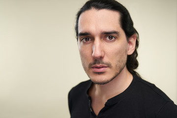 Portrait of latino handsome man with long black hair and black t shirt in studio