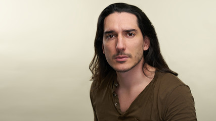 Portrait of latino handsome man with long black hair and green t shirt in studio