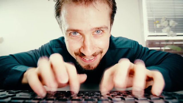 Man extreme fast typing and stare into camera 4K. Low angle view from behind the keyboard with a male person face in focus while typing.