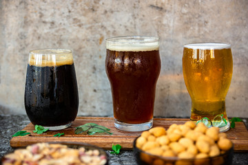 tres tipos de cerveza rubia, roja y negra, sobre una tabla de madera, con mani, fondo de metal