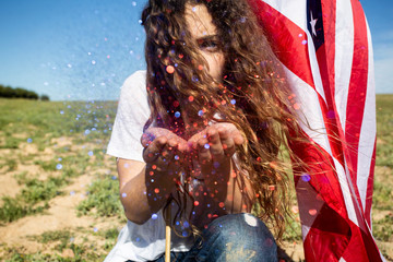 Woman with American flag blowing glitter in field