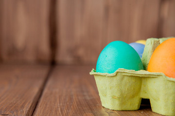 Colorful Easter eggs in box on wooden background with copy space