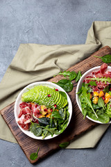 Low carbs bowl. Fresh salad with green spinach, rucola, avocado an ham serrano in white bowl, gray background, top view
