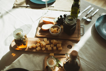 wooden table with cheese, bread, jam, grapes, olives and wine in a stylish setting. sunny, retro and vintage breakfast concept