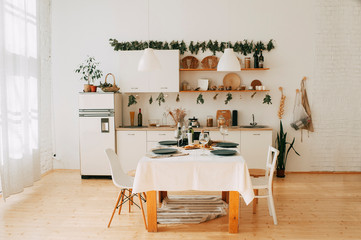 Cozy, warm, white kitchen in scandinavian style with wooden table and chairs. Stylish kitchen interior design. Home renovation. Vintage style kitchen interior. Party table