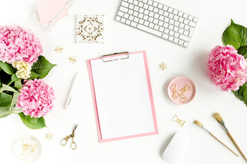 Stylized women's desk. Workspace with clipboard, computer, bouquet hydrangea, accessories on white background. Flat lay. Top view.