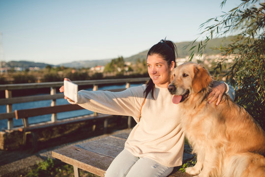Smiling young woman taking a selfie with her dog at the waterfront