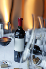 bottle of red wine, a glass of wine and a decanter on a table with a white tablecloth.