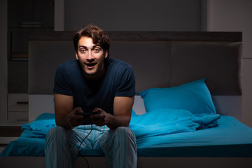 Fototapeta premium Young man playing computer games at night in bed