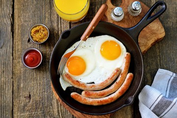 Fried eggs and thin sausages in a cast iron skillet. Breakfast. Top view.