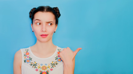 Funny cute girl on a blue studio background. Bright emotional female portrait. Woman raises one...
