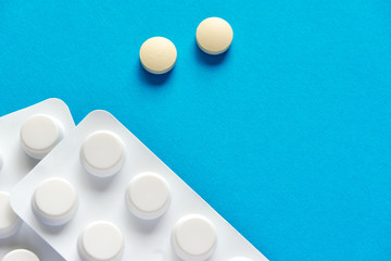 Two round and white prescription tablets or pills and pill strip on blue or teal background with copy space for use as a template   