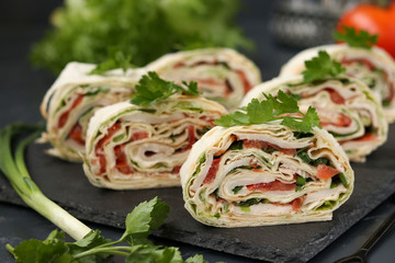 Lavash roll with smoked chicken, tomatoes, cheese and greens located on a dark background