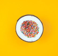 Coconut full of colorful sprinklers on yellow background