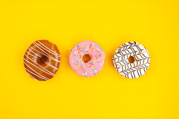 three multi-colored donuts on yellow background