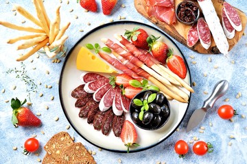 Antipasti snacks - sausage, homemade grissini with jamon, olives, strawberries, capers, cherry tomatoes, white wine, dried tomatoes and more. Top view. 
