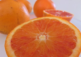 close-up of red Sicilian orange Tarocco on a light gray surface. Whole and sliced oranges with juicy pulp.