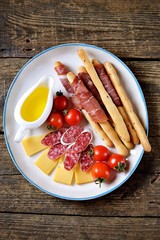 Antipasti snacks - sausage, homemade grissini with jamon, cheese, cherry tomatoes and olive oil. Top view. 