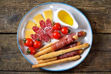 Antipasti snacks - sausage, homemade grissini with jamon, cheese, cherry tomatoes and olive oil. Top view. 