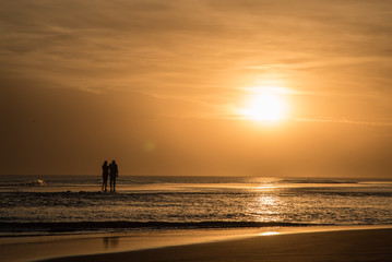 Fototapeta premium Couple walking on the beach at sunset, reflection of the sun on the sea, sunset orange