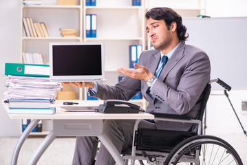 Young handsome employee in wheelchair at the office