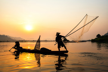 Asia fisherman net using on wooden boat casting net sunset or sunrise in the Mekong river - Silhouette fisherman