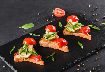 Appetizer bruschetta with vegetables, tomatoes and spices on black shale board over black stone...
