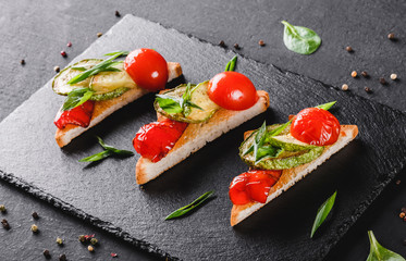 Appetizer bruschetta with vegetables, tomatoes and spices on black shale board over black stone background. Healthy food concept