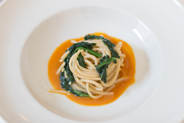 Close up on a white dish with italian food pasta an orange juice and vegetables.
