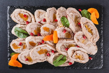 Assorted meat, stuffed chicken roll, meat roll with pomegranate, greens on black shale background. Meat appetizer, food concept. Top view, flat lay