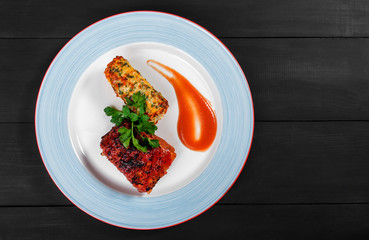 Grilled meat steak with grilled corn in cheese and greens in plate on dark wooden background. Hot Meat Dishes. Top view, flat lay