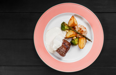 Roasted potatoes with beef meat, herbs, broccoli and sauce in plate on dark wooden background. Hot Meat Dishes. Top view, flat lay