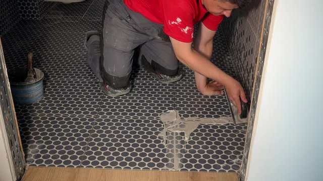 Worker putting fugue on floor in bathroom. Grouting ceramic tiles