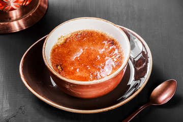 Creme brulee or french vanilla cream dessert with caramelised sugar with tea on dark background.