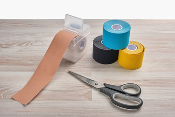 Rolls of colored kinesio tape with a pair of scissors on a wooden background