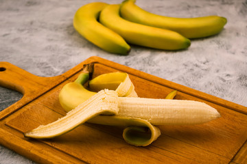 A whole banana, half peeled. Wooden background. Exotic fruits.