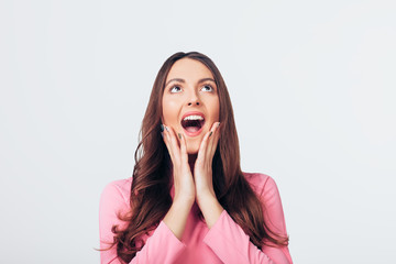 Young happy and surprised woman looking up and holds cheeks by hands isolated on white backround