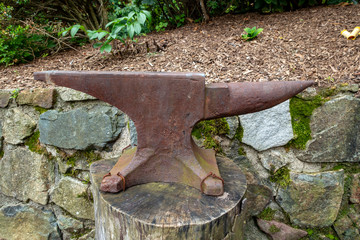 Rusty anvil nailed to a tree stump with a rock wall in the background
