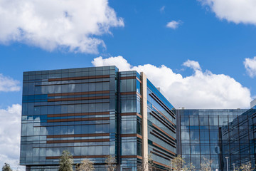 An office building with mirror like windows in the day light with white fluffy clouds in the blue sky.