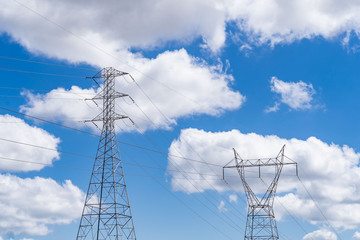 Large high tension power lines with cables and structures showing on a parlty cloudy and sunny day with blue skies