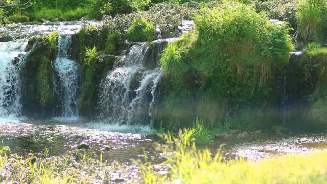 Scenic waterfall on a tufa dam, River Lathkill, Peak District, England. Camera pan.
