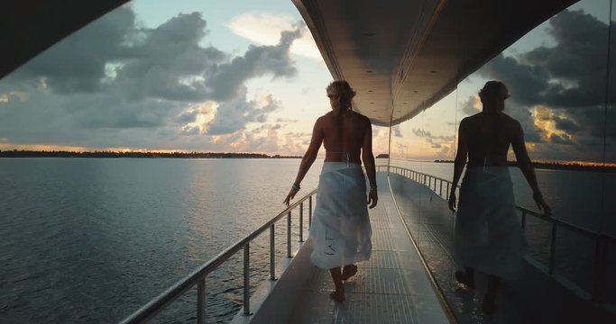 Slow motion of young woman walking on a sailing yacht boat on ocean water at scenic sunset panorama.