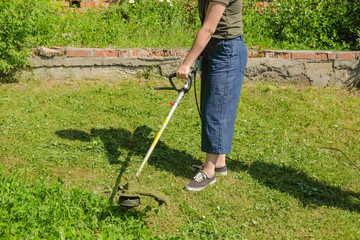 Girl mows the grass trimmer. Portrait of a close-up hand mowing grass. Cut the lawn.