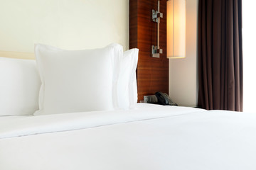 White pillows on bed covered with white sheets by the window