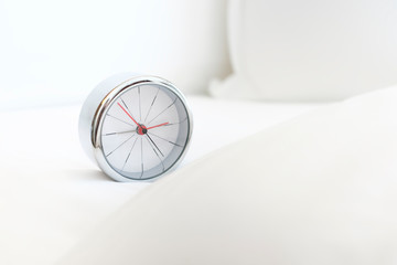 Alarm clock on the bed covered with white sheets