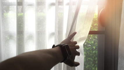 Male hand wearing digital watch opening the white curtain with morning sunlight effect.