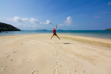 young man with red bagpack is jumping on white beach and blue sky during happy vacation day in Koh kham, Trat, Thailand.