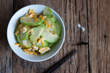 Fresh chayote fruits (Sechium edulis) stir fried with egg and garlic in bowl on wood background