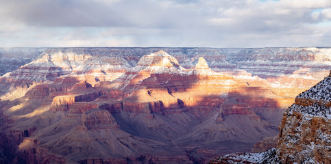 An evening winter panorama of the Grand Canyon with snow in the high elevation and dramatic sunlight and shadows being cast into the canyon.