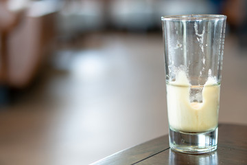 Selective focus empty glass of sparkling nitro cold brew coffee remaining the frothy foam that served at coffee shop wooden table with blurred background.